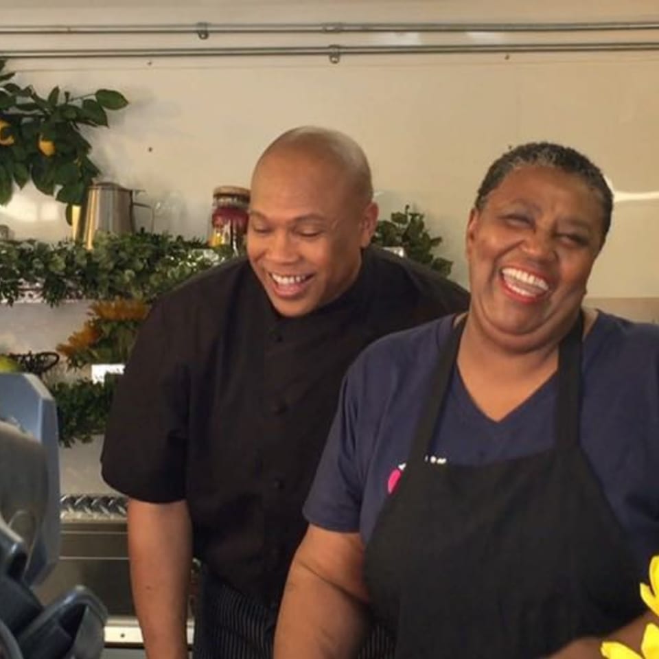 Two smiling chefs, a man and a woman, stand together in a kitchen setting.