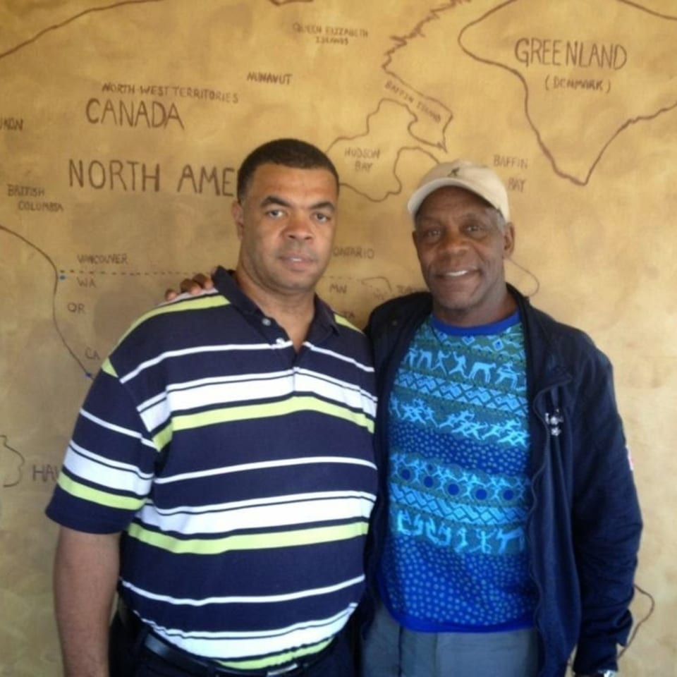 Two men stand smiling in front of a large map of North America, Canada, and Greenland.