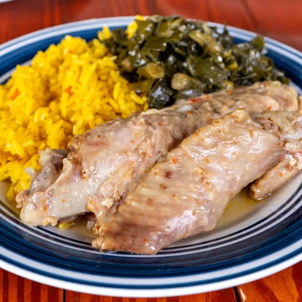 Sisters of the New South's turkey wings with yellow rice and collard greens on a blue-striped plate.