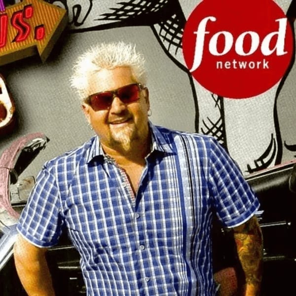 Guy Fieri smiling in a blue plaid shirt and red sunglasses, with a Food Network logo.