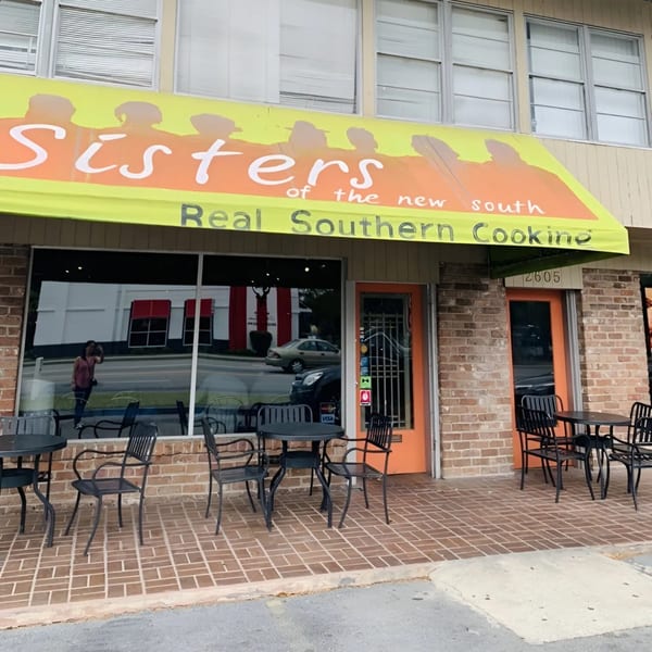 Exterior of Sisters of the New South, a soul-food restaurant, with outdoor seating and a yellow awning.