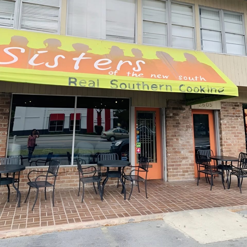 Exterior of Sisters of the New South, a soul-food restaurant, with outdoor seating and a yellow awning.