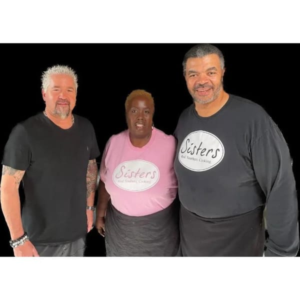 Guy Fieri poses with two Sisters of the New South staff members in branded shirts.