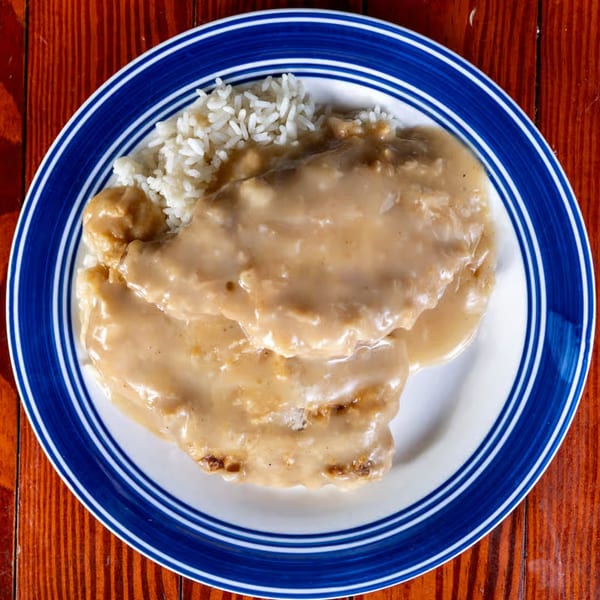Two pieces of fried chicken covered in gravy with a side of white rice on a blue and white plate.