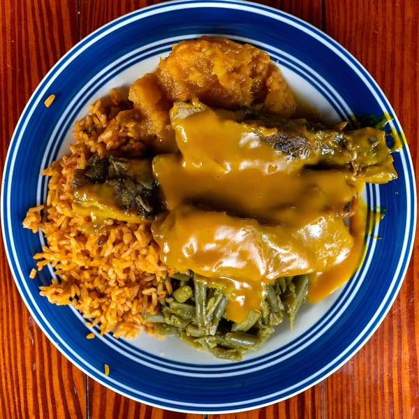 Soul food plate with smothered pork chops, rice, green beans, and candied yams on a blue and white plate.