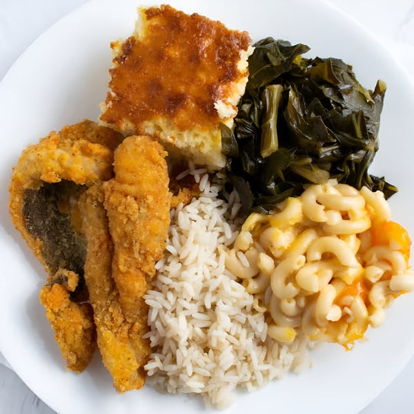 A soul food platter with fried fish, rice, macaroni and cheese, collard greens, and cornbread.