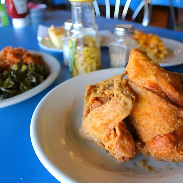 Golden-brown fried chicken, collard greens, and sweet potatoes on a blue table at Sisters of the New South.