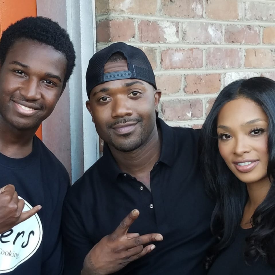 Three people, two men and one woman, smiling and posing together against a brick wall.